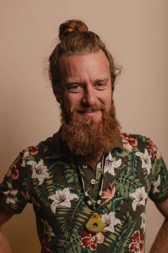 Photo d'un homme avec barbe et cheveux en chignon, portant un t-shirt à motifs floraux.